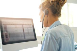 A woman wearing a headset phone looks at a computer screen