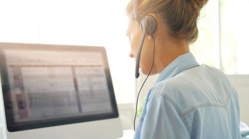 A woman wearing a headset phone looks at a computer screen